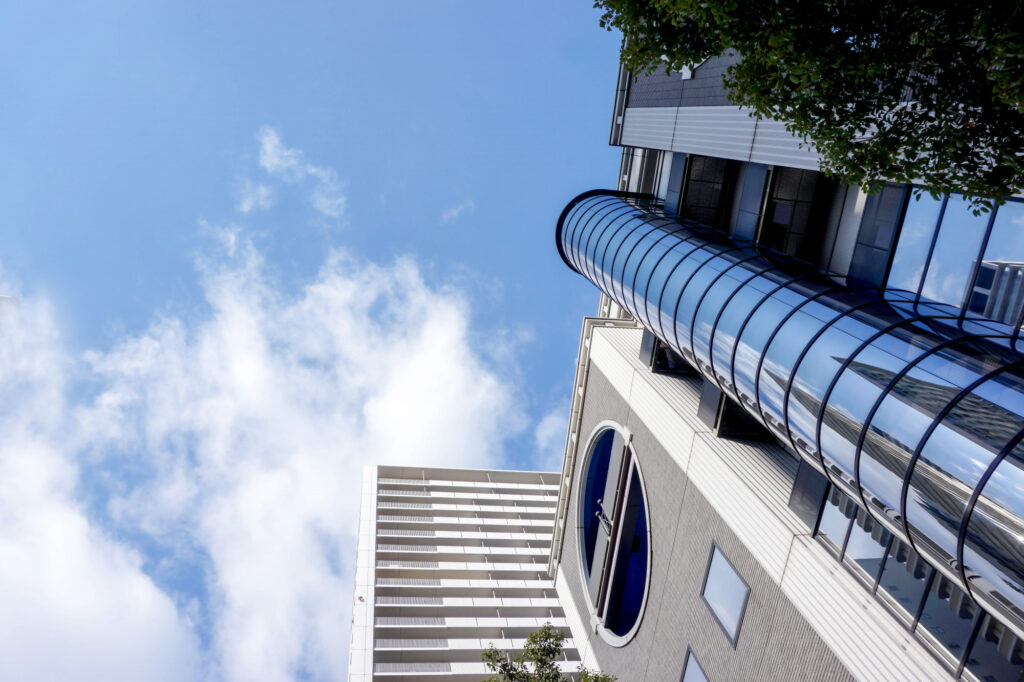Vue en contre-plongée d'un immeuble moderne avec passerelle vitrée incurvée sous un ciel bleu